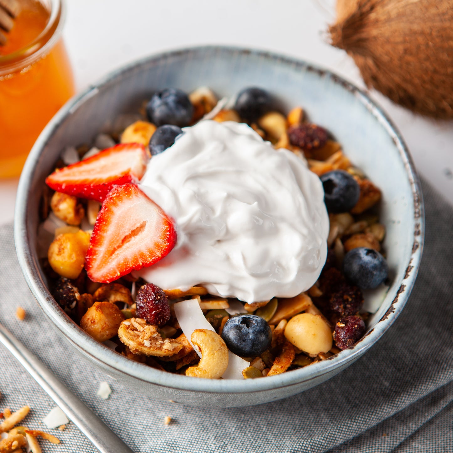Bowl of granola with yogurt, strawberries, and blueberries on a light surface.