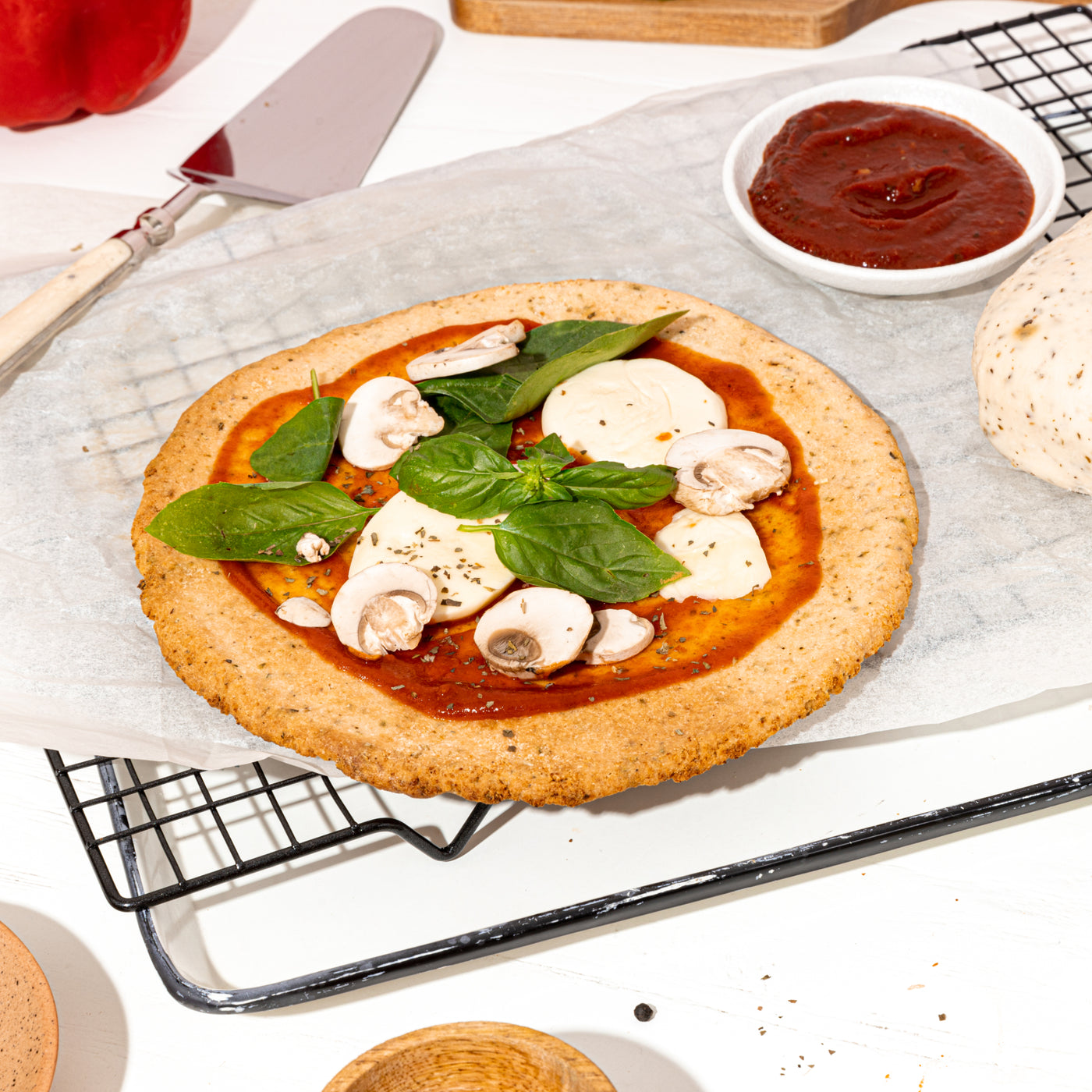 Unbaked pizza with tomato sauce, cheese, and mushrooms on a cooling rack.