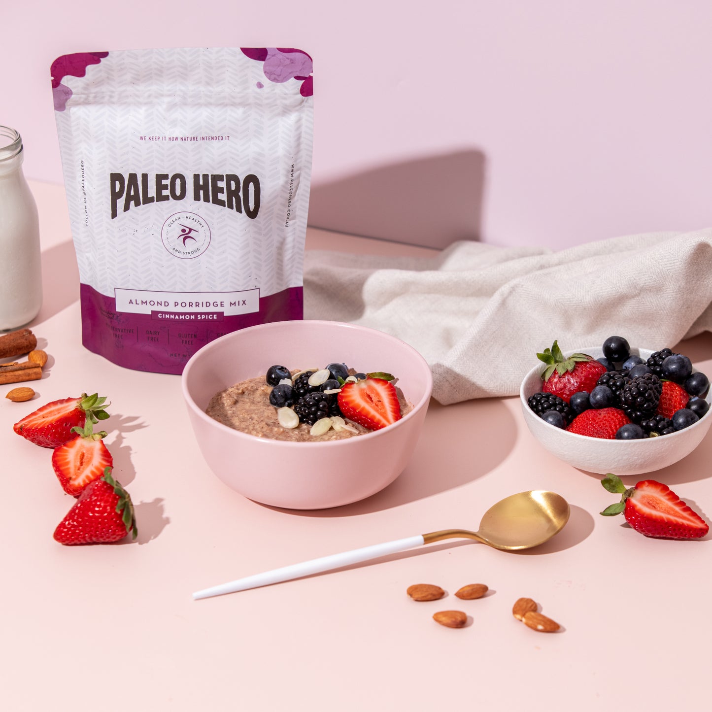 Paleo Hero almond forriege mix package with a bowl of porridge and berries on a pink background