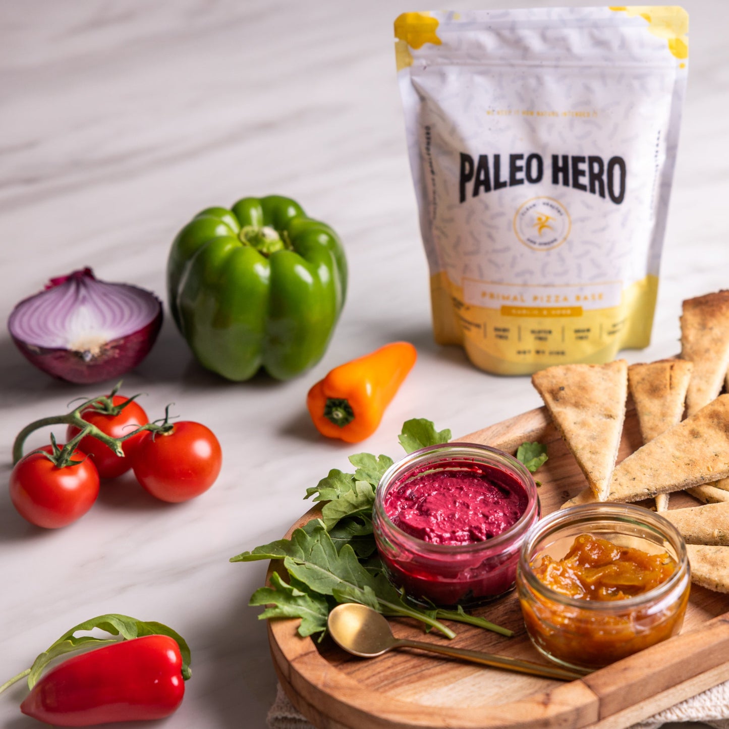 Platter of pita bread, hummus, and vegetables with Paleo Hero packaging on a light background