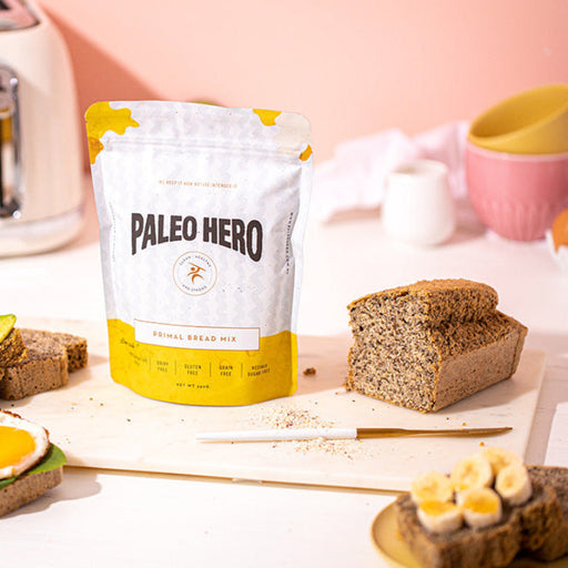 Bag of Paleo Hero Bread Mix on a countertop with a loaf of bread against a pink backdrop and a toaster to its left